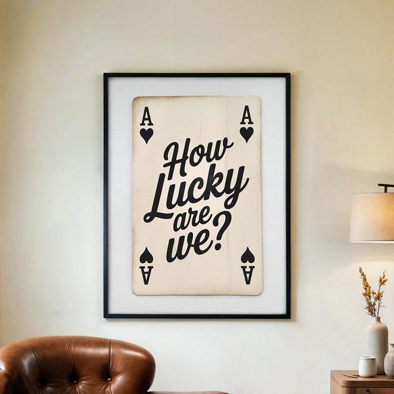 Op de afbeelding: Een ingelijste kunstdruk met een speelkaartontwerp. De kaart is een Ace of Spades in vintage-stijl met de tekst "How Lucky are we?" in zwart script. De print zit in een zwart frame.