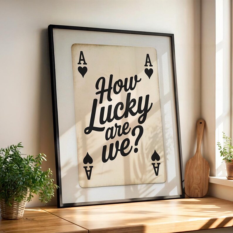 Op de afbeelding: Ingelijste kunstafdruk van een schoppenaas. De kaart bevat de tekst "How Lucky are we?" in een stijlvol zwart lettertype. De schoppenaaskaart heeft vier zwarte hartsymbolen en de letter "A" in elke hoek. De print zit in een zwart frame.