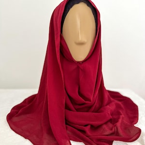 May include: A burgundy chiffon hijab, a lightweight and flowy headscarf, draped over a mannequin head.