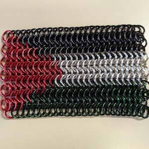 May include: A small chainmail flag with the colors of the Palestinian flag. The flag is made of black, white, red, and green chainmail rings.