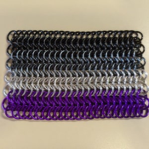 May include: A black, white and purple chainmail bracelet, made of metal rings, resembling the asexual pride flag.
