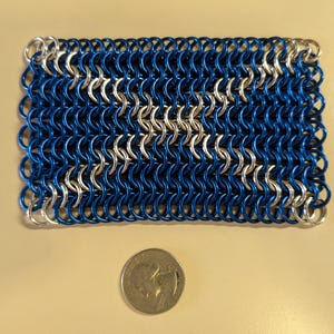 May include: A blue and silver chainmail weave, resembling a small rectangular rug. The chainmail is made of metal rings, with the blue rings being larger than the silver rings.