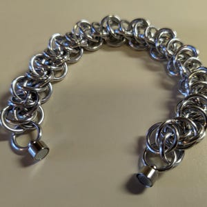 May include: A silver chain bracelet with magnetic clasps. The bracelet is made of interlocking metal rings.