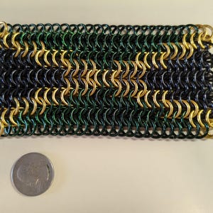 May include: A green, gold, and black chainmail bracelet. The chainmail is made of small metal rings that are interlocked to create a flexible and durable fabric.