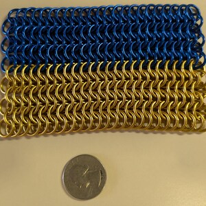 May include: A close-up of a blue and gold chainmail, a type of woven metal mesh, with a coin for scale.