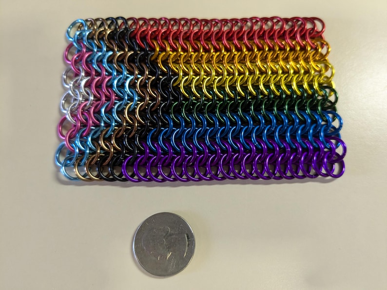 May include: A rainbow-colored chainmail bracelet made of small metal rings. The bracelet is made in the colors of the pride flag, with each color represented by a row of rings. The bracelet is about 2 inches wide and 4 inches long.