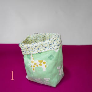 May include: A green fabric storage bin with a white floral print on the top edge and a green and yellow giraffe print on the bottom. The bin is sitting on a pink surface.