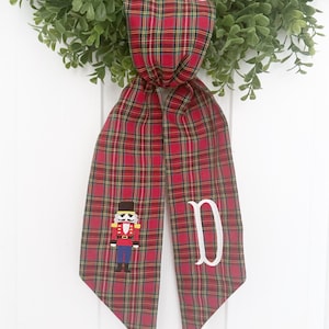 May include: Red and green plaid ribbon with a white embroidered nutcracker and the letter "D".