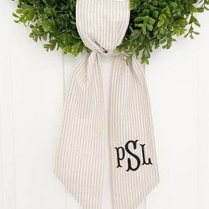 May include: A beige and white striped fabric door hanger with the monogram "PSL" embroidered in black.