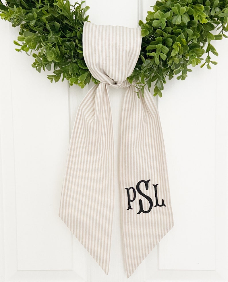 May include: A beige and white striped fabric door hanger with the monogram "PSL" embroidered in black.