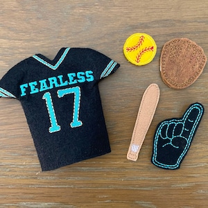 May include: A black felt jersey with the word "Fearless" and the number "17" embroidered in turquoise blue.  There are also felt baseball-themed accessories, including a baseball, a bat, and a foam finger.