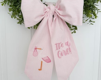 May include: Pink and white striped bow with an embroidered stork carrying a pink bundle and the text "It's a Girl!"