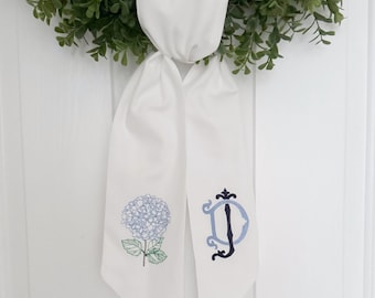 May include: White fabric ribbon with a blue hydrangea flower and a black embroidered letter "D" on each side.