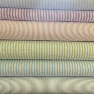 May include: A stack of six rolls of striped fabric in various colors, including pink, peach, green, blue, and white.