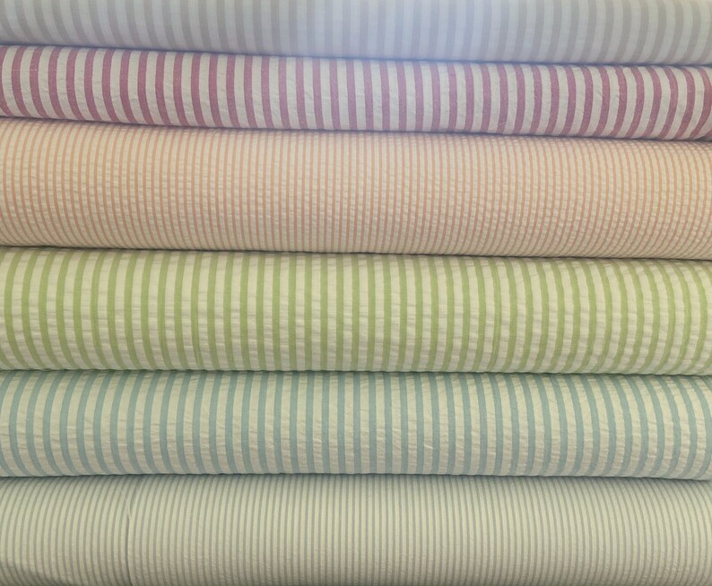 May include: A stack of six rolls of striped fabric in various colors, including pink, peach, green, blue, and white.