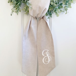 May include: A beige linen wedding ceremony ribbon with a white embroidered letter "S" on one end.