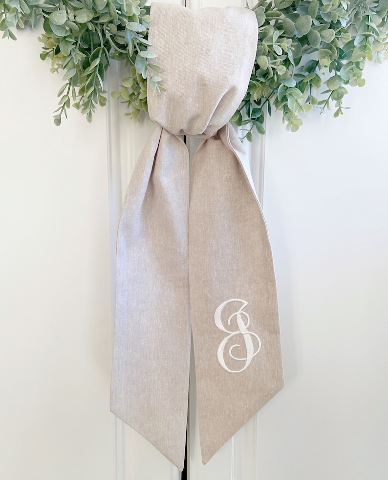 May include: A beige linen wedding ceremony ribbon with a white embroidered letter "S" on one end.
