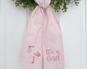 May include: Pink and white striped fabric bow with an embroidered pink stork carrying a pink bundle and the text "It's a Girl!"