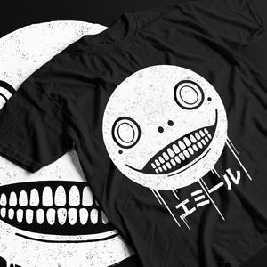 Könnte beinhalten: Schwarzes T-Shirt mit einer weißen Grafik eines lächelnden Gesichts mit großen Augen und Zähnen. Das Design enthält japanischen Text und eine Used-Optik. Das Shirt besteht aus einem weichen Material.