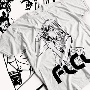 Puede incluir: Camiseta blanca con una ilustración en blanco y negro de una persona sosteniendo una cámara. El texto "FLCU" está impreso en negro en la esquina inferior derecha de la camiseta.