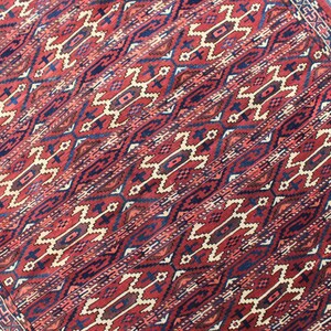 May include: A red, blue, and cream patterned rug with a geometric design. The rug has a fringe border.