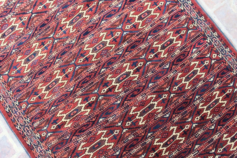 May include: A red, blue, and cream patterned rug with a geometric design. The rug has a fringe border.