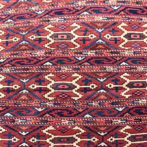 May include: A close-up of a red, blue, and white patterned rug with a geometric design. The rug has a traditional Persian style.