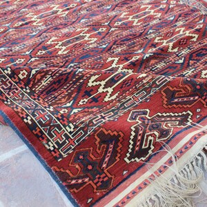 May include: A red, blue, and white patterned rug with fringe. The rug has a geometric design and is made of wool.