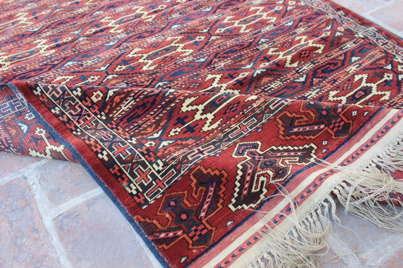 May include: A red, blue, and white patterned rug with fringe. The rug has a geometric design and is made of wool.