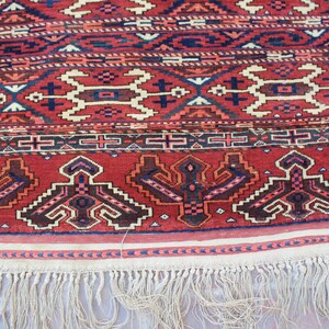 May include: A red, blue, and white patterned rug with a fringe border. The rug has a traditional design with geometric shapes and floral motifs.