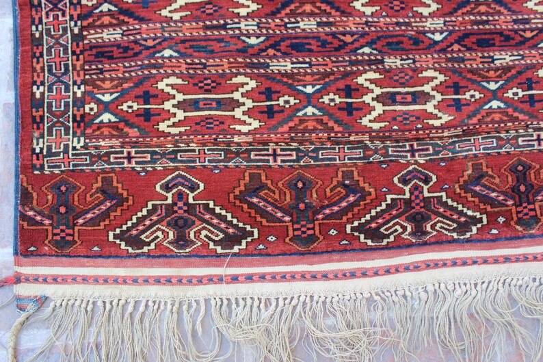 May include: A red, blue, and white patterned rug with a fringe border. The rug has a traditional design with geometric shapes and floral motifs.