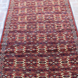 May include: A red, blue, and cream colored rug with a geometric pattern. The rug has a fringe on the top and bottom.