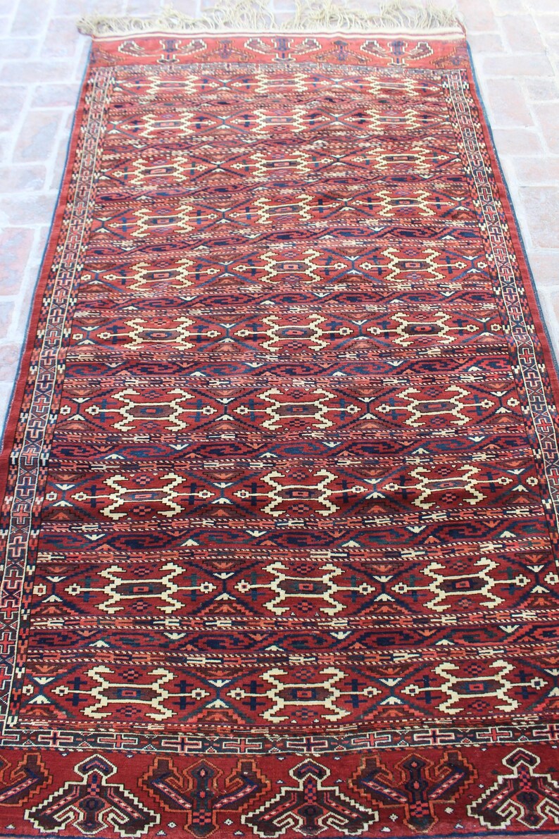 May include: A red, blue, and cream colored rug with a geometric pattern. The rug has a fringe on the top and bottom.
