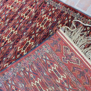 May include: A red and blue patterned rug with a fringe border. The rug has a traditional design with geometric shapes and intricate details.