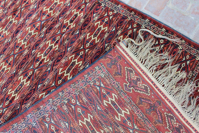 May include: A red and blue patterned rug with a fringe border. The rug has a traditional design with geometric shapes and intricate details.