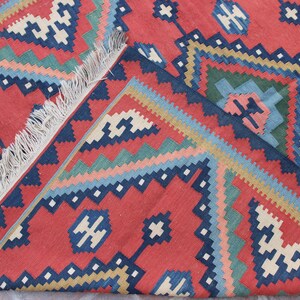 May include: A red, blue, green, and white patterned rug with fringe. The rug has a geometric design.