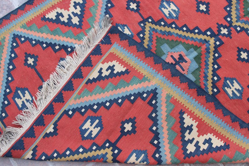 May include: A red, blue, green, and white patterned rug with fringe. The rug has a geometric design.