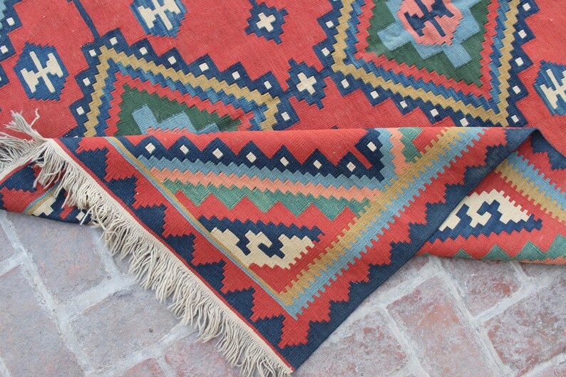 May include: A red, blue, green, and cream colored woven rug with a geometric pattern. The rug has fringe on all sides.