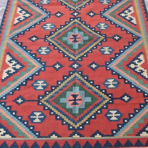 May include: A red, blue, green, and cream colored rug with a geometric pattern. The rug has a fringe border.