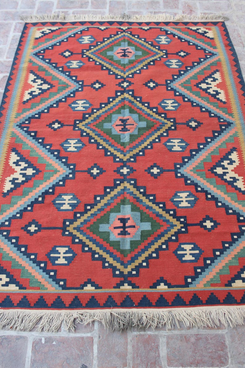 May include: A red, blue, green, and cream colored rug with a geometric pattern. The rug has a fringe border.