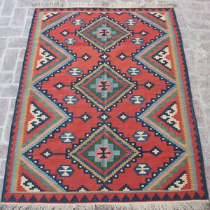 May include: A red, blue, green, and cream colored rug with a geometric pattern. The rug has a fringe border.