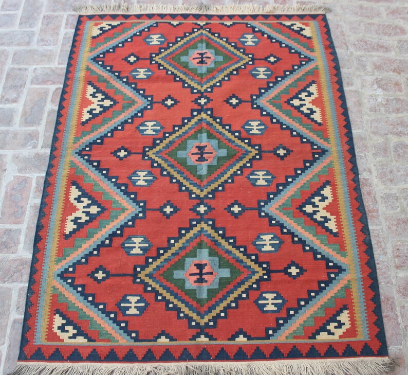 May include: A red, blue, green, and cream colored rug with a geometric pattern. The rug has a fringe border.
