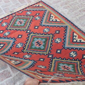 May include: A red, blue, green, and cream colored rug with a geometric pattern. The rug has a fringe border.