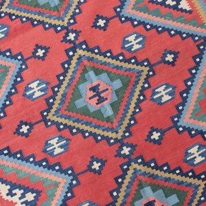 May include: A red, blue, green, and cream colored rug with a geometric pattern. The rug has a diamond shape in the center with smaller diamond shapes surrounding it.