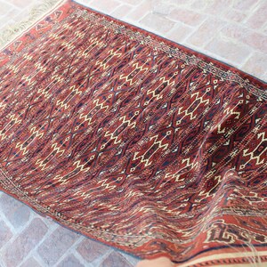 May include: A red, black, and cream patterned rug with a geometric design. The rug is folded in half and has a fringe border.