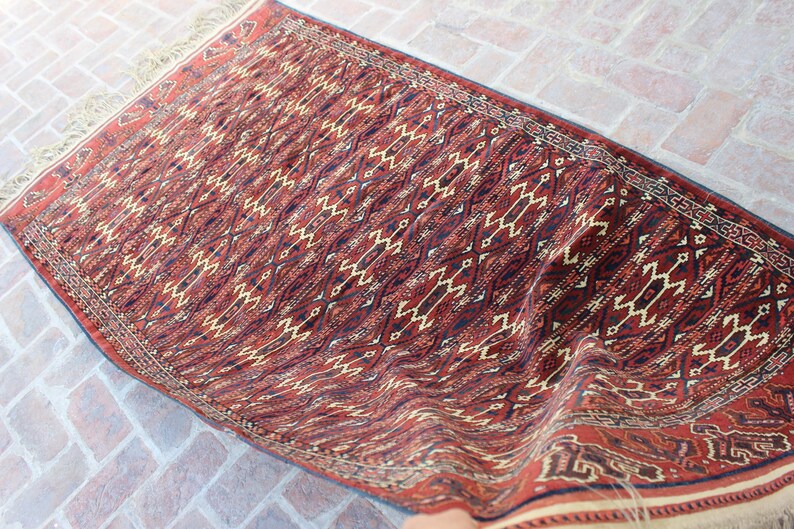 May include: A red, black, and cream patterned rug with a geometric design. The rug is folded in half and has a fringe border.