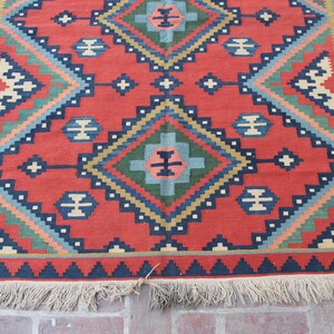 May include: A red, blue, green, and cream colored rug with a geometric pattern. The rug has a fringe border.