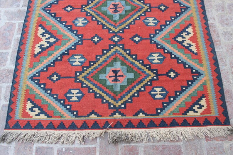 May include: A red, blue, green, and cream colored rug with a geometric pattern. The rug has a fringe border.