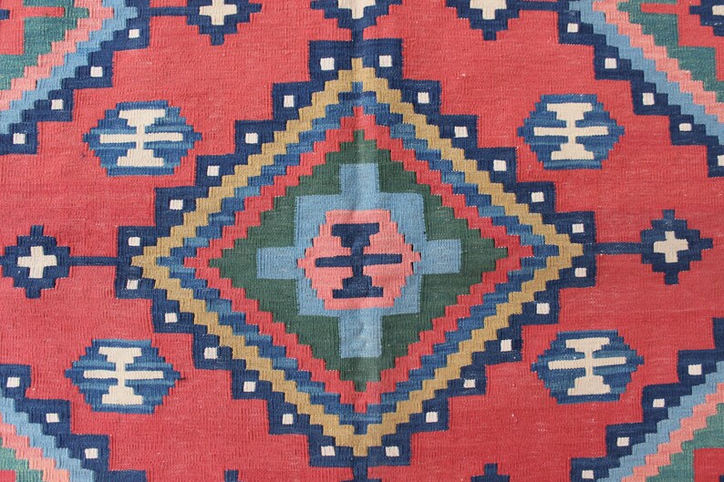 May include: A close-up of a red, blue, green, and beige patterned rug with a diamond-shaped design in the center.