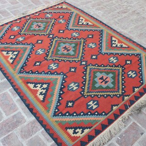 May include: A red, blue, green, and cream colored rug with a geometric pattern. The rug has a fringe border.